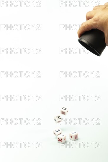 White poker dice with black and red markings roll out of a black cup held by a dealer on a white