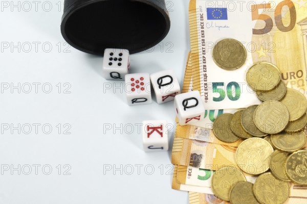 Poker dice spilling from a black cup onto a pile of fifty euro banknotes and coins, symbolizing