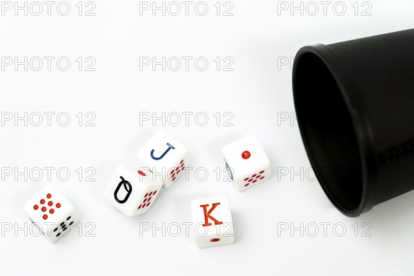 Poker dice spilling from a black dice cup onto a white background, representing gambling and games