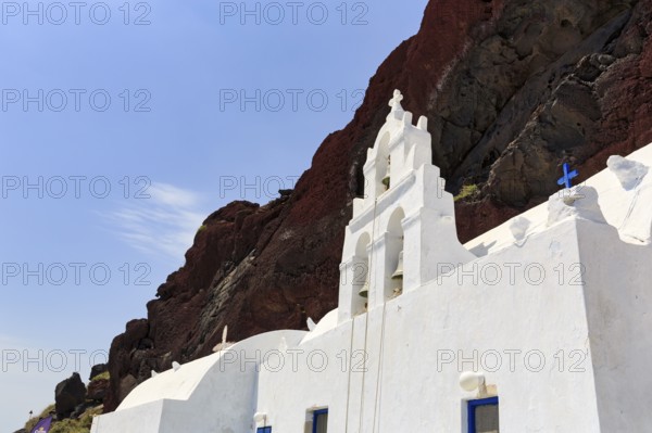 Agios Nikolaos Mavrorachidi, chapel with bell tower in front of red rock face, volcanic rock,