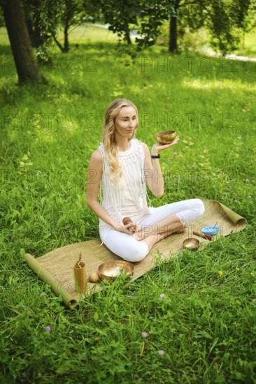 A woman engages in a calming meditation session, holding a singing bowl while seated on a mat in a