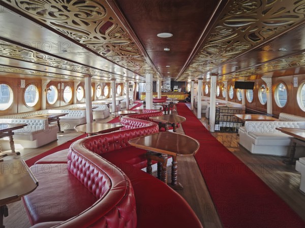 Luxurious ship interior with long hall, red carpets, leather couches and curved wooden tables.