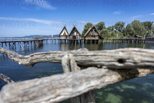Pile dwellings protrude into the water, embedded in a picturesque lake and hilly landscape,