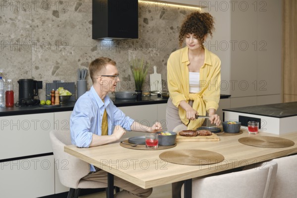 In a contemporary kitchen, a couple is sharing a moment as one partner serves a meal while the