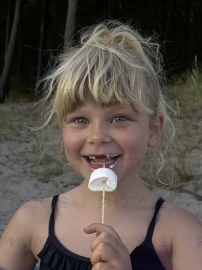 Happy blonde 7 year old Scandinavian girl eating marshmallows outdoors in Ystad, SkÃ¥ne County,