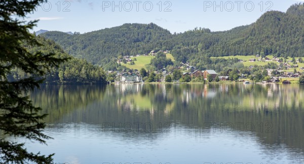 Tranquil lake with surrounding village and wooded hills on the shore reflected in the water,