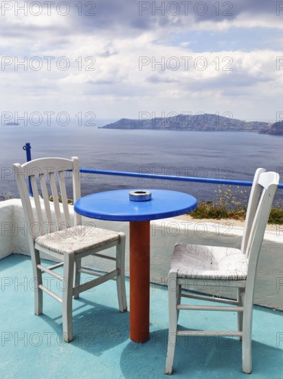 Blue table and two white wooden chairs on a terrace with sea view, typical view of the volcanic