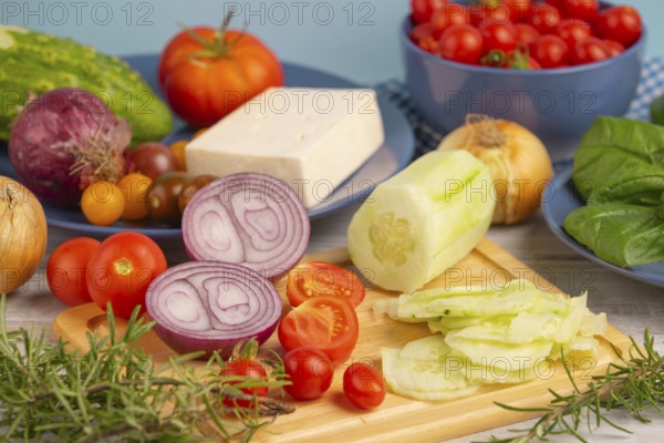 Fresh and sliced vegetables with feta on a wooden board, surrounded by basil and rosemary, rustic