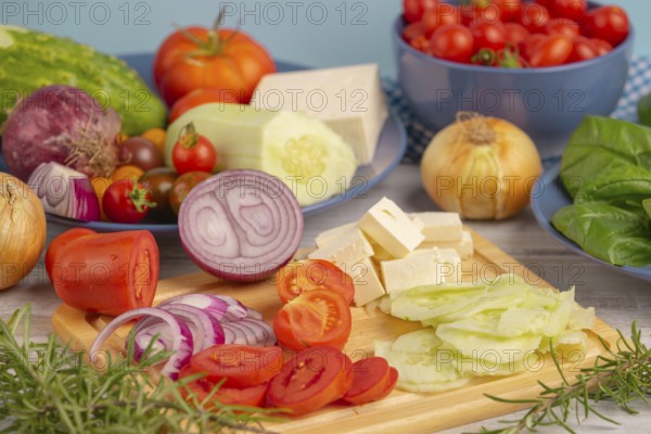 Fresh and sliced vegetables with feta on a wooden board, surrounded by basil and rosemary, rustic