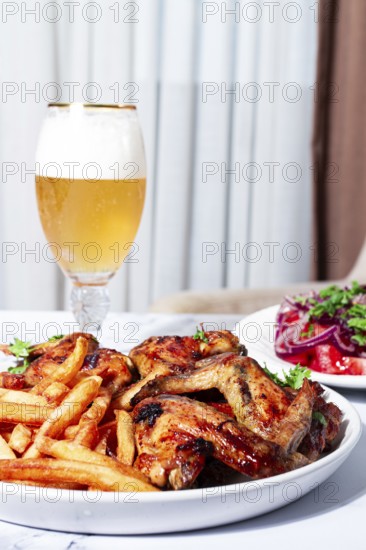 Delicious barbecue chicken wings, with French fries, salad and a refreshing drink, at a cozy table,