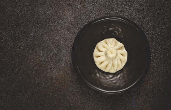 One khinkali, on a black plate, top view, cooking concept, Georgian cuisine
