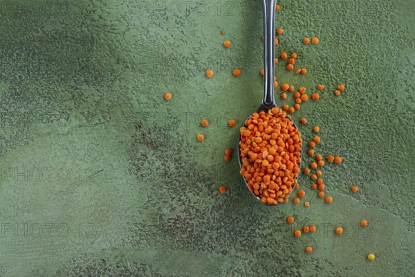 Bright orange lentils spill from a silver spoon onto a textured green surface, highlighting the