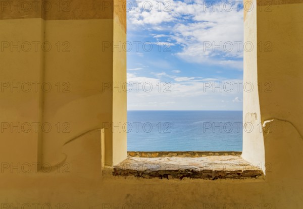 Sunny mediterranean sea scenery seen through a window opening in a historic wall seen in Liguria,