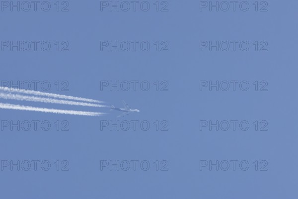 Boeing 747 Jumbo jet passenger aircraft in flight in a blue sky with vapour trails or contrails