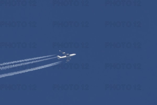 Boeing 747 Jumbo jet passenger aircraft in flight in a blue sky with vapour trails or contrails