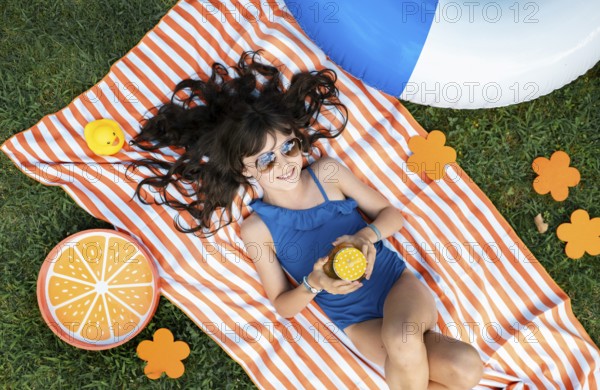 Girl, 10, with sunglasses in a blue swimming costume, lying relaxed in the meadow with a cocktail