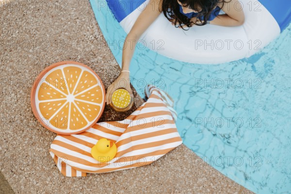 Girl with a swimming tyre in the pool, a striped bath towel, a swimming duck, a cocktail and an
