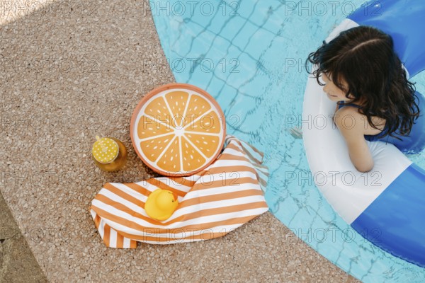 Girl with a swimming tyre in the pool, a striped bath towel, a swimming duck, a cocktail and an