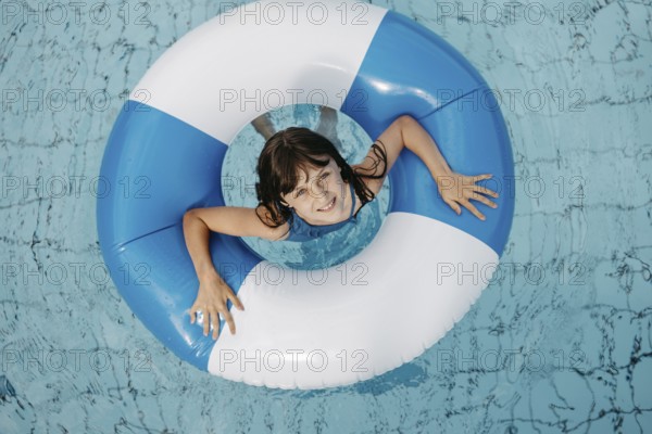 Girl, 10, in the pool, looks out of a blue and white striped swimming tyre