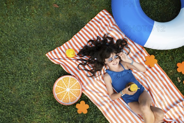 Girl, 10, with sunglasses in a blue swimming costume, lying relaxed in the meadow with a cocktail