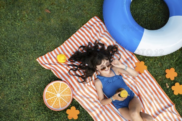 Girl, 10, with sunglasses in a blue swimming costume, lying relaxed in the meadow with a cocktail