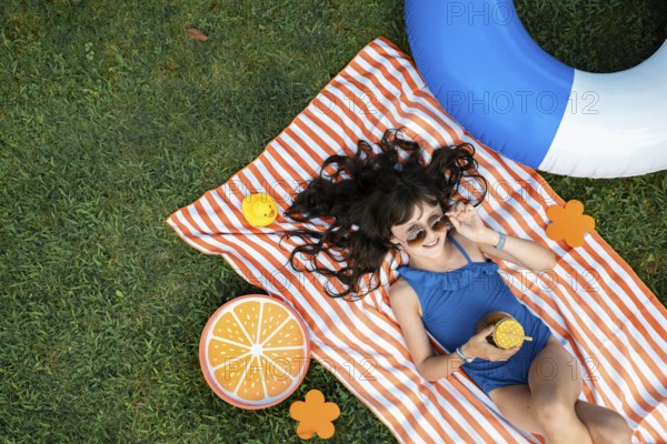 Girl, 10, with sunglasses in a blue swimming costume, lying relaxed in the meadow with a cocktail