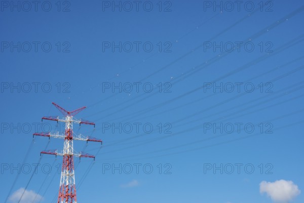 An extremely high electricity electricity electricity pylon, marked white and red, on the banks of