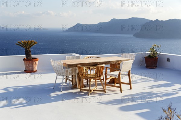 Wooden table and various chairs on a white terrace by the sea, view of the caldera, Oia, Santorini,