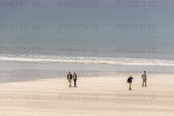 Group of people walking in the sunshine on a sandy beach with rolling waves at the sea, Crozon