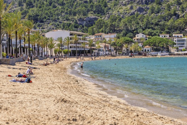 Sand beach with tourists at a tourist resort with houses at the shore line and palm trees a sunny