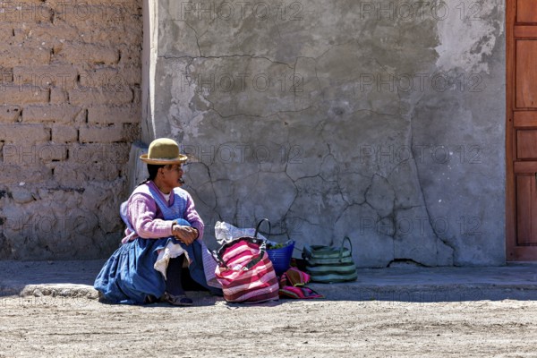 Woman in traditional dress sitting on the floor next to colourful bags in front of a wall,