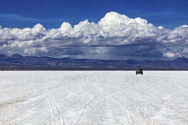 An off-road vehicle drives across an endless salt flat under a sky full of clouds, The endless
