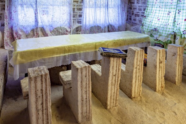 Long stone table with matching stone chair set in a bright, rustic room with patterned curtains,