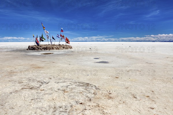 Flags in a vast salt lake under a clear blue sky with scattered clouds, international flags in the