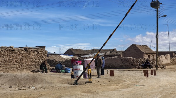 People in a desert town with clay-like buildings and a street lamp under a blue sky, A village on