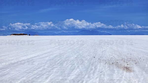Vast salt flat with a mountain range on the horizon and clouds under a clear sky, The endless