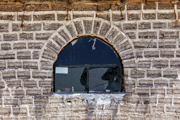 The rustic window with reflection is located in a curved brick wall, A wall made of salt bricks in
