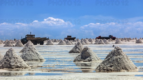 Lorries and salt hills on a reflective salt flat under a blue sky and clouds, The endless expanses