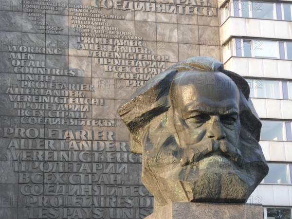 Stone bust of Karl Marx in front of a building with multilingual communist writings, Karl Marx