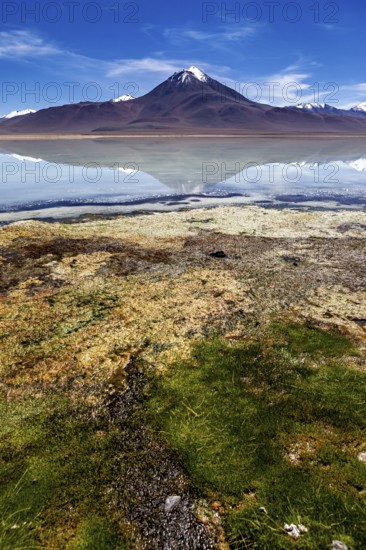 Volcano in front of a clear lake whose surface reflects the summit and the blue sky, The Laguna