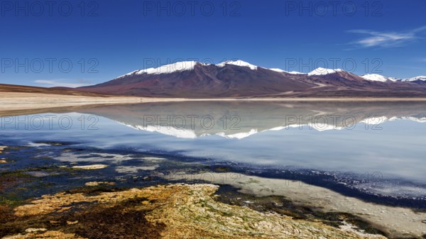 Mountain landscape with a lake whose clear surface reflects the snow-covered peaks under a clear
