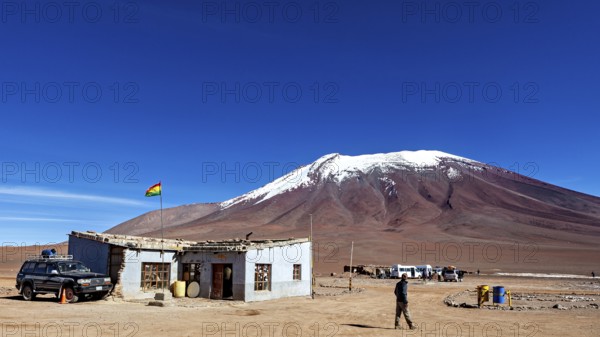 A remote mountain region with a simple building and a vehicle, overlooked by a clear blue sky, The