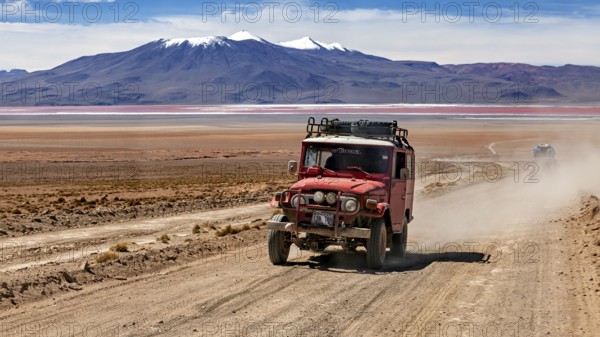A jeep drives dusty on a desert road with mountains in the background, off road in the landscape of