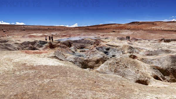 Landscape with geysers in a desert, two people on the horizon, clear blue sky, The mud volcanoes