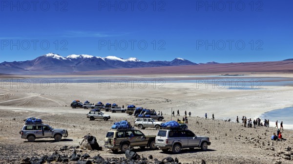 Several off-road vehicles parked in a desert landscape with mountains and snow-capped peaks under a