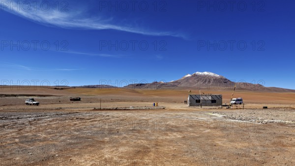 Vast, lonely desert landscape with a small building and snow-capped mountains in the background,