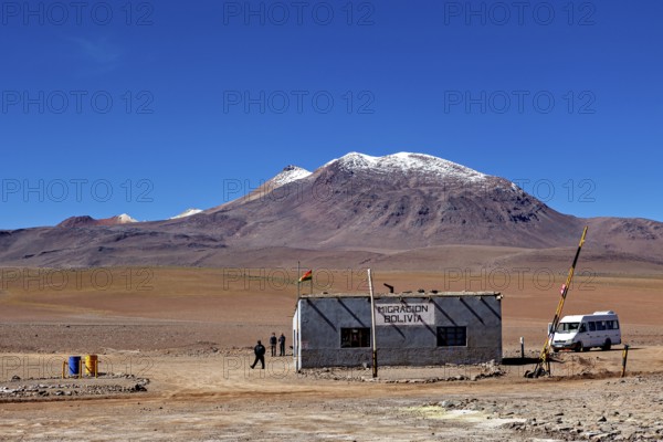 A small migration building in a vast desert landscape with snow-capped mountains, The border