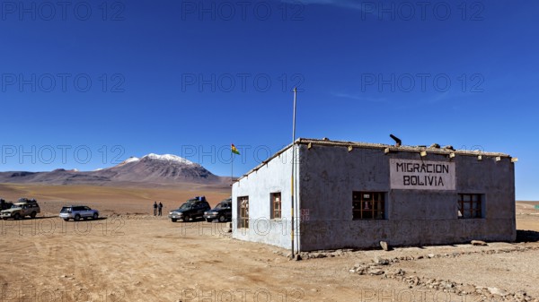 A small border building in a barren landscape with snow-capped mountains in the background, The