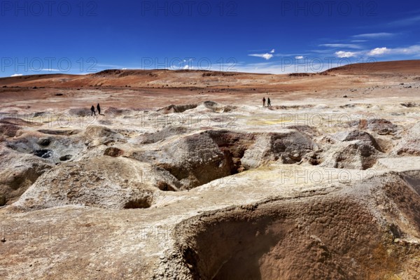 Vast, barren rocky landscape in the desert, two people on the horizon, blue sky, the mud volcanoes
