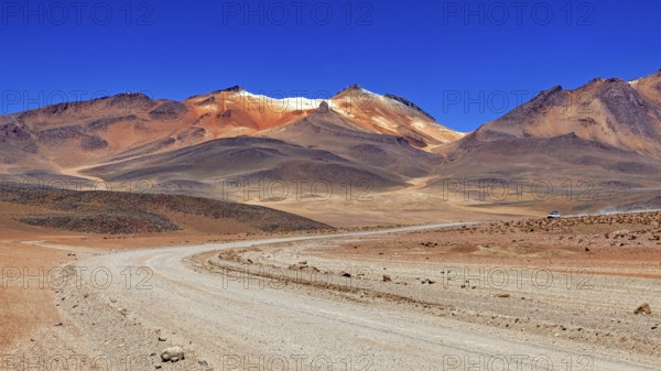 A sandy road winds its way through a vast, barren landscape under a bright blue sky, The landscape